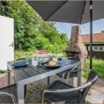 Terrasse mit Tisch, Stühlen und Sonnenschirm. Hintergrund: Steinofen und grüne Landschaft.