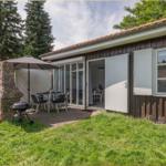 Haus mit Terrasse, Grill und Sitzgruppe im Freien. Glasfront öffnet sich ins Innere.