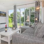 Wohnzimmer mit Sofa, Couchtisch und Fernseher. Durchführung zur Terrasse mit Blick auf Grünflächen.