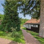 Wohnhaus mit Holzfassade und Ziegeldach. Gartenweg und große Nadelbäume sichtbar.