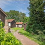 Haus mit Steinmauer, Gartenweg und Bäumen unter blauem Himmel.