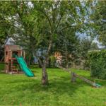 Hinterhof mit Spielplatz, Schaukel und Apfelbaum. Grasfläche und Bepflanzung sichtbar.