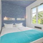 Schlafzimmer mit Bett, blauer Tapete und Fenster mit Blick auf Bäume.