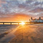 Sonnenuntergang über Strand und Pier mit weißem Gebäude im Hintergrund.