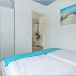 Schlafzimmer mit Doppelbett, weißer Kleiderschrank und Strandbild an der Wand.