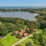 Häuser mit roten Dächern liegen am See, umgeben von Wäldern und Grünflächen.