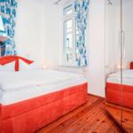 Bedroom with red bed, wooden floor, and blue curtains on windows.