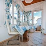 Dining table with chairs and blue-white tablecloth in front of windows with balcony view.