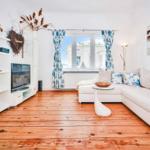 Living room with white sofa, wooden floor, and TV unit. Windows with blue curtains.