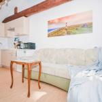 Living room with sofa, kitchenette, and wooden ceiling beams. Wall art shows lighthouse.