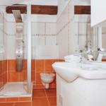 Bathroom with shower, sink, and toilet. Orange tiles and wooden beams.