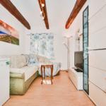 Living room with sofa, kitchenette, and TV. Wooden beams on the ceiling.