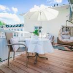 Terrace with table, chairs, umbrella, and hanging chair. Wooden deck and white railing.