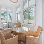 A room with sofa, round table, and chairs. Large windows with view of buildings.