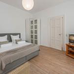 Bedroom with bed, TV, and closet. Wooden floor and white walls.