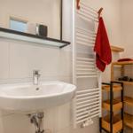 Bathroom with sink, mirror, towel rack, and wooden shelf.