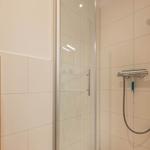 Shower with glass enclosure, shower head, and wooden shelf with towel.