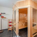 Sauna mit Holzverkleidung und Sitzbänken. Nebenraum mit Ständer und Wegweiser.