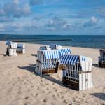 Strand mit weißen Strandkörben und blau-weißem Streifenmuster, Blick auf das Meer.