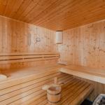 Holzsauna mit Sitzbänken, Körbchen und Thermometer an der Wand.