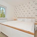 Schlafzimmer mit Bett, Nachttisch und Fenster mit Blick auf Garten.