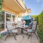 Terrace with table, chairs, and grill. Green hedge and beach chair in background.