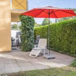 Terrace with red umbrella, lounge chair, and grill. Surrounded by green hedges.