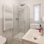 Bathroom with shower, sink, and toilet. Window with curtain.
