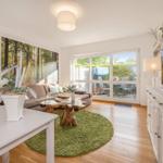 Living room with sofa, green rug, and TV. Entrance to terrace with garden.