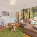 Living room with sofa, dining table, and forest wall mural. Wooden floor and green rug.