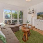 Living room with sofa, wooden table, and TV. Entrance to terrace with garden.
