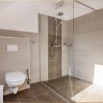 Bad mit Dusche, Toilette und Toilettenpapierhalter an der Wand.
