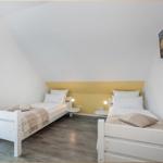 Zwei Einzelbetten mit Matratzen und Kissen, Wand-TV und Fenster mit Vorhängen.