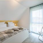 Schlafzimmer mit Doppelbett, gelbem Kopfteil und großem Fenster mit Vorhang.