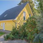 Gelbes Haus mit dunklem Dach und Gartenweg. Auf der Wand steht Haus Sonnenschein.