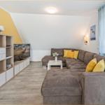 Ein Wohnzimmer mit braunem Sofa, gelben Kissen und einem Fernseher auf einem Schrank.