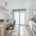 Essbereich mit Tisch, Stühlen und Küchenzeile. Fenster mit Vorhängen und Karte an der Wand.