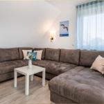 Ein Wohnzimmer mit einem großen braunen Sofa, einem weißen Tisch und einem Fenster mit hellblauen Vorhängen.