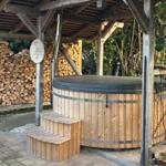 Holzgefäss-Hot Tub unter Pavillon mit Holzstapel im Hintergrund.