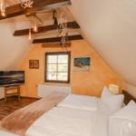 Schlafzimmer mit Dachschrägen, Bett, Fernseher und Fenster.