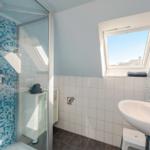 Bad mit Dusche, Waschbecken und Dachfenster. Wände mit blauen Fliesen.