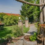 Garten mit Pflanzen, Steingartenweg und Holzpfosten. Blick auf das Haus mit rotem Dach.