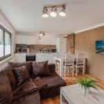 Wohnküche mit braunem Sofa, Esstisch und Fernseher an der Wand.