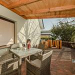 Terrasse mit Sitzgruppe, Grill und Holzüberdachung. Pflasterboden und Holzwände.