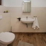 Badezimmer mit Toilette, Waschbecken und Spiegel. Holzfußboden und weiße Fliesen.