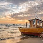 Ein hölzernes Fischerboot liegt am Strand, im Hintergrund See und Himmel bei Sonnenuntergang.