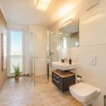 Badezimmer mit Dusche, Waschbecken und Toilette. Fenster mit Blick nach draußen.