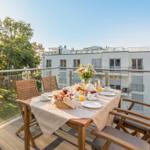 Terrasse mit Tisch, Stühlen und Frühstück. Blick auf Gebäude und Bäume.