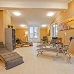 Raum mit Liegen, Schrank und Fenstern. Wandbild und Bodenfliesen sichtbar.