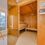 Sauna mit Holzverkleidung, Sitzbänken und Heizung. Fenster mit Blick nach draußen.